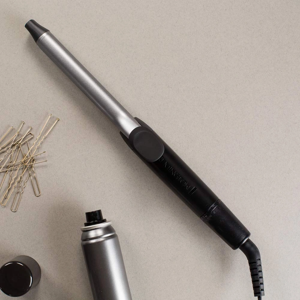 Ein Lockenstab, Haarnadeln und eine Haarspraydose liegen auf einem grauen Hintergrund.