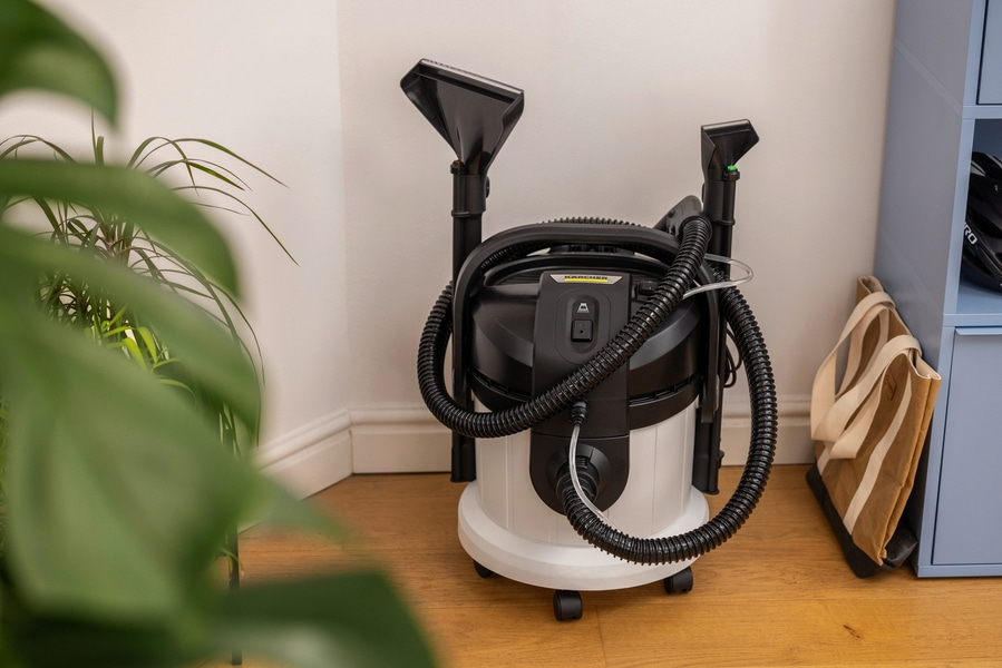 Kärcher-Staubsauger, schwarz-weiß, mit Zubehör, steht im Raum, neben Pflanze und Tasche.
