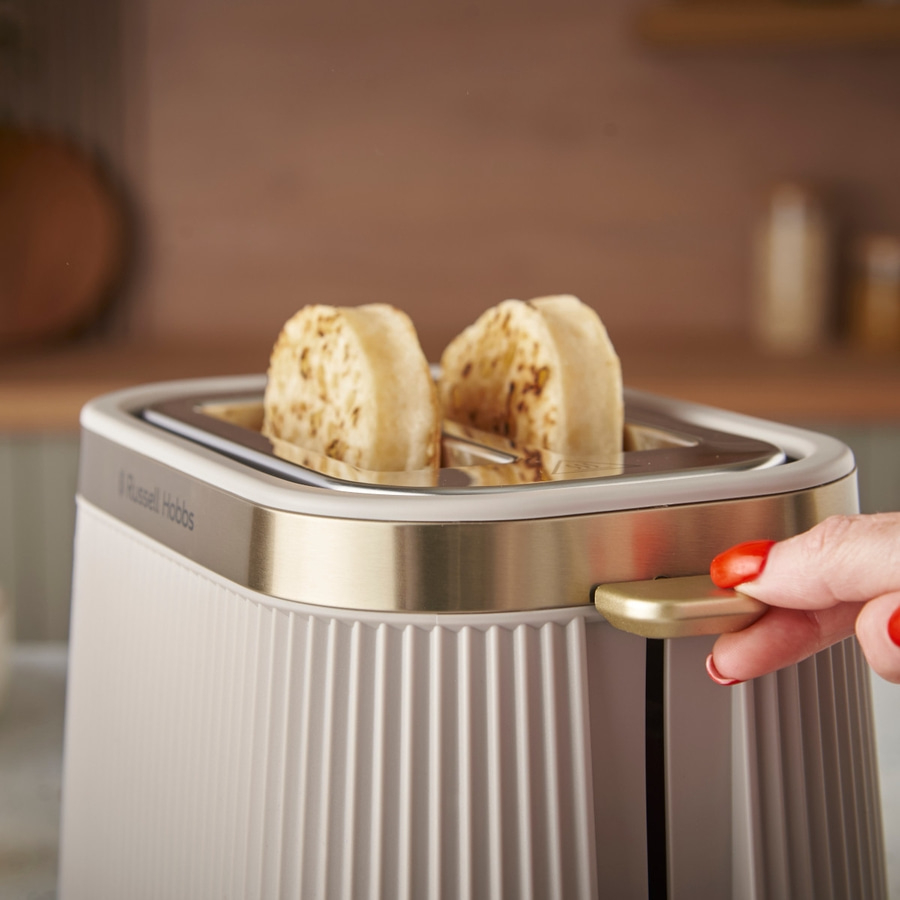 Toaster mit Toast, goldfarbenen Akzenten und einer Hand, die den Hebel betätigt