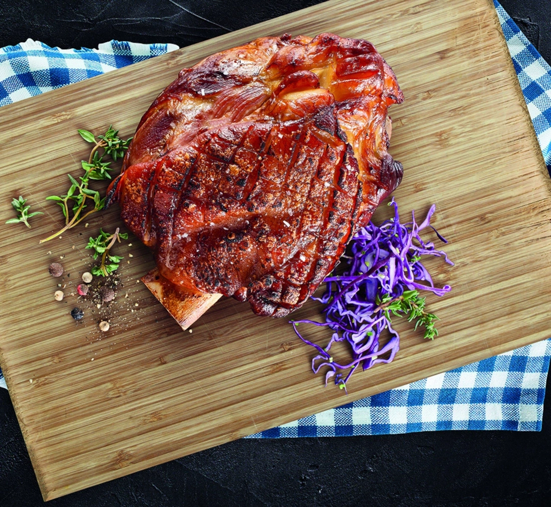 Ein gebratenes Schweinebein mit Beilagen auf einem Holzbrett