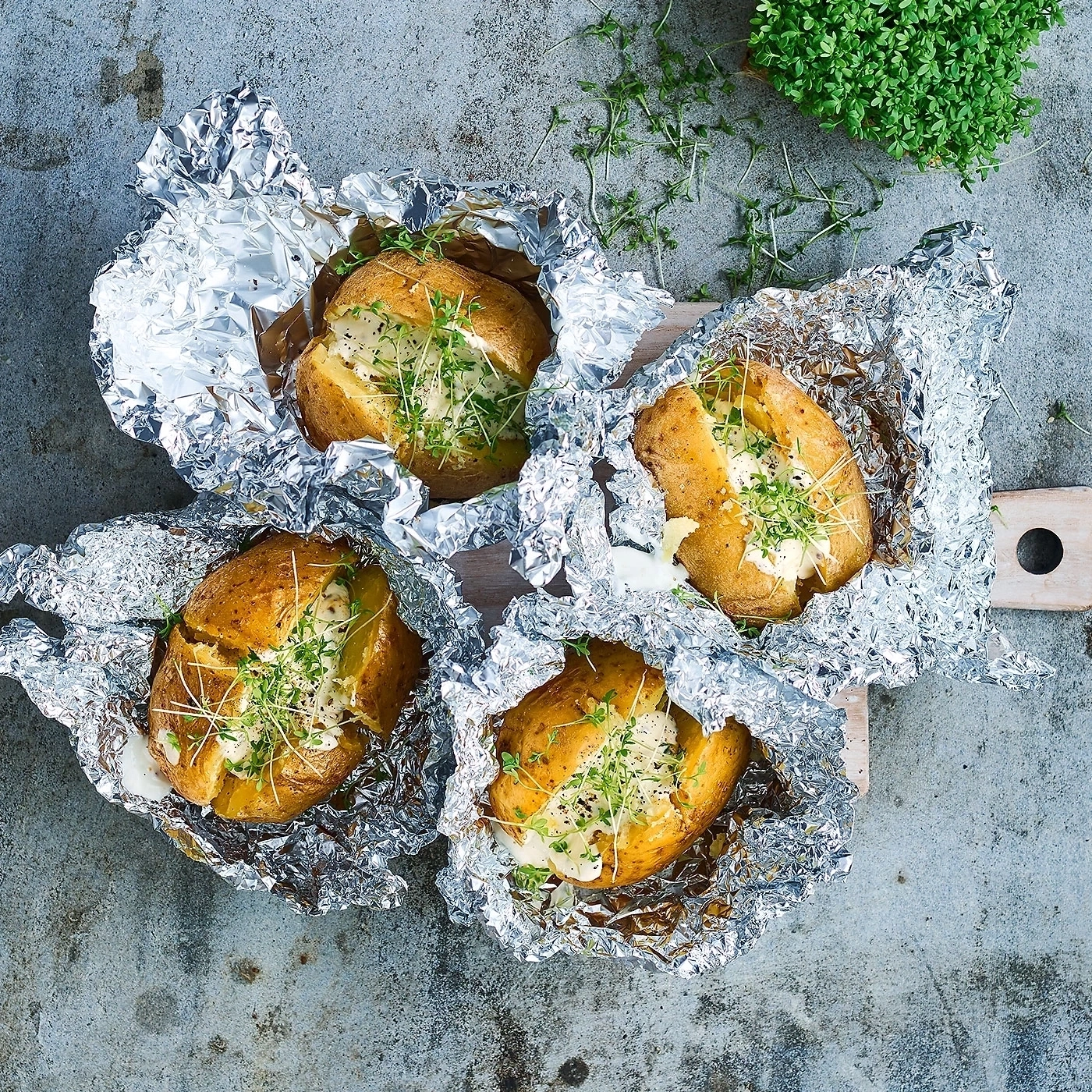 Gegrillte Kartoffeln in Folie mit Kräutern und Sauce auf einem Brett