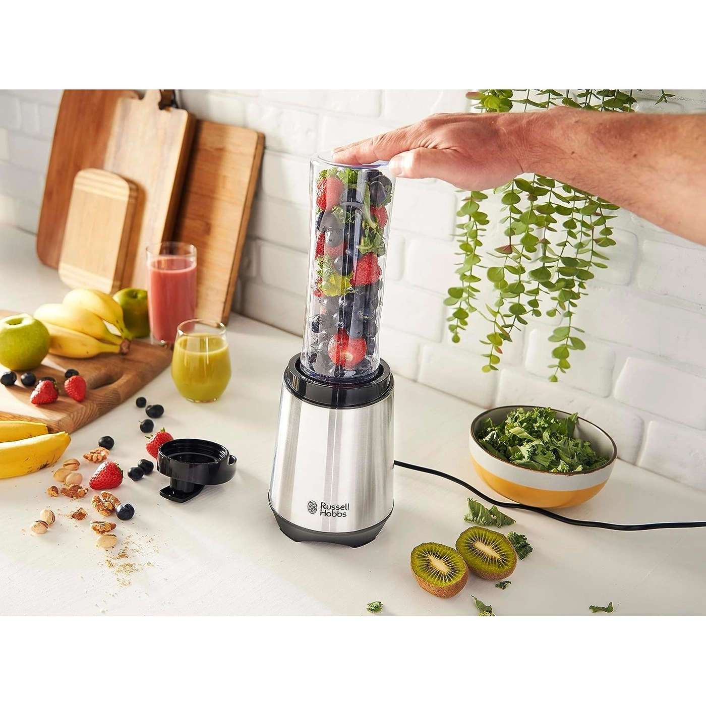 Ein Smoothie-Maker mit Früchten, Kiwi, Gemüse und einer Hand, die ihn bedient.