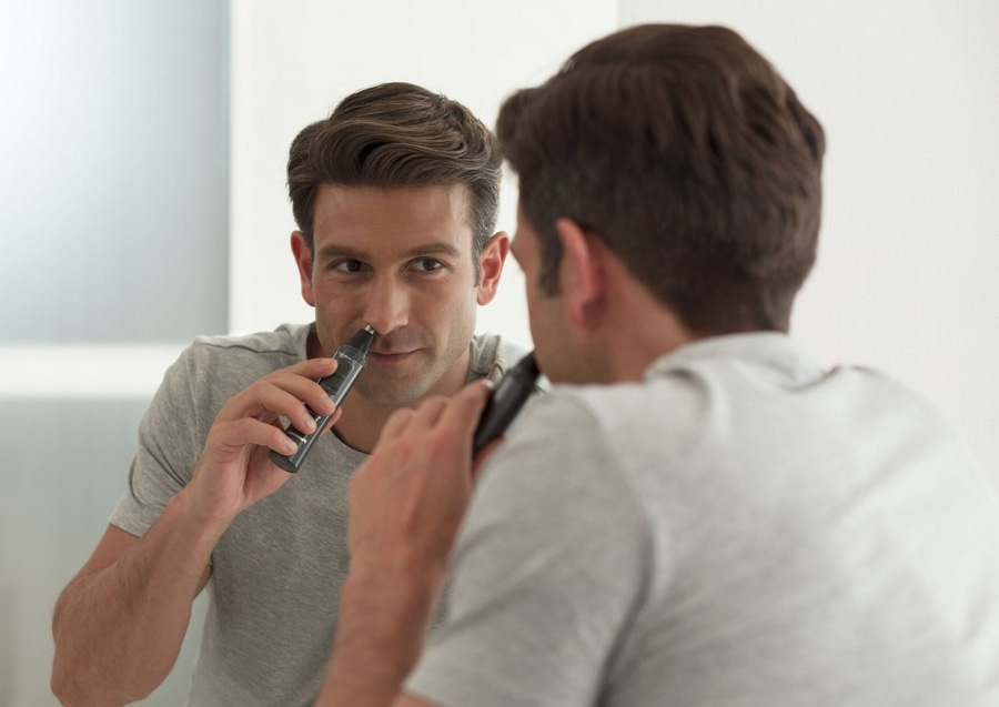 Mann rasiert sich vor dem Spiegel die Nase mit einem Trimmer. Nahaufnahme.