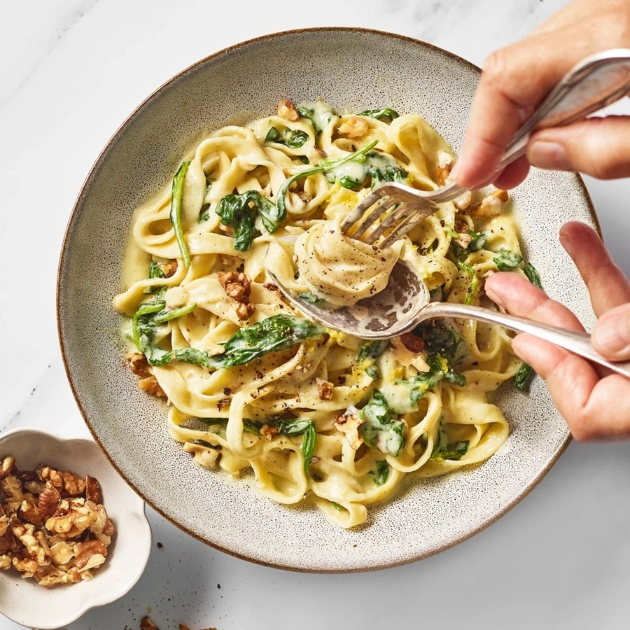 Pasta mit Spinat, Walnüssen und cremiger Sauce auf einem Teller.