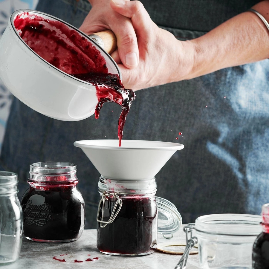 Person gießt Marmelade in Gläser. Hausgemachte Konfitüre wird abgefüllt.