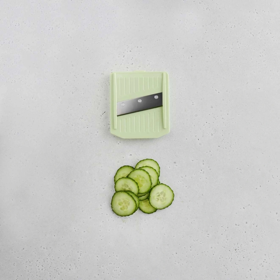 Gurkenscheiben und Gemüseschneider auf hellem Untergrund. Küche, Kochen, Gemüse.