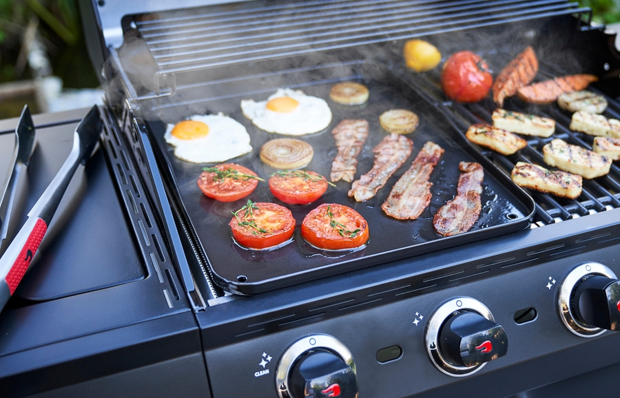 Ein Grill mit Essen, darunter Eier, Speck und Tomaten, wird zubereitet.