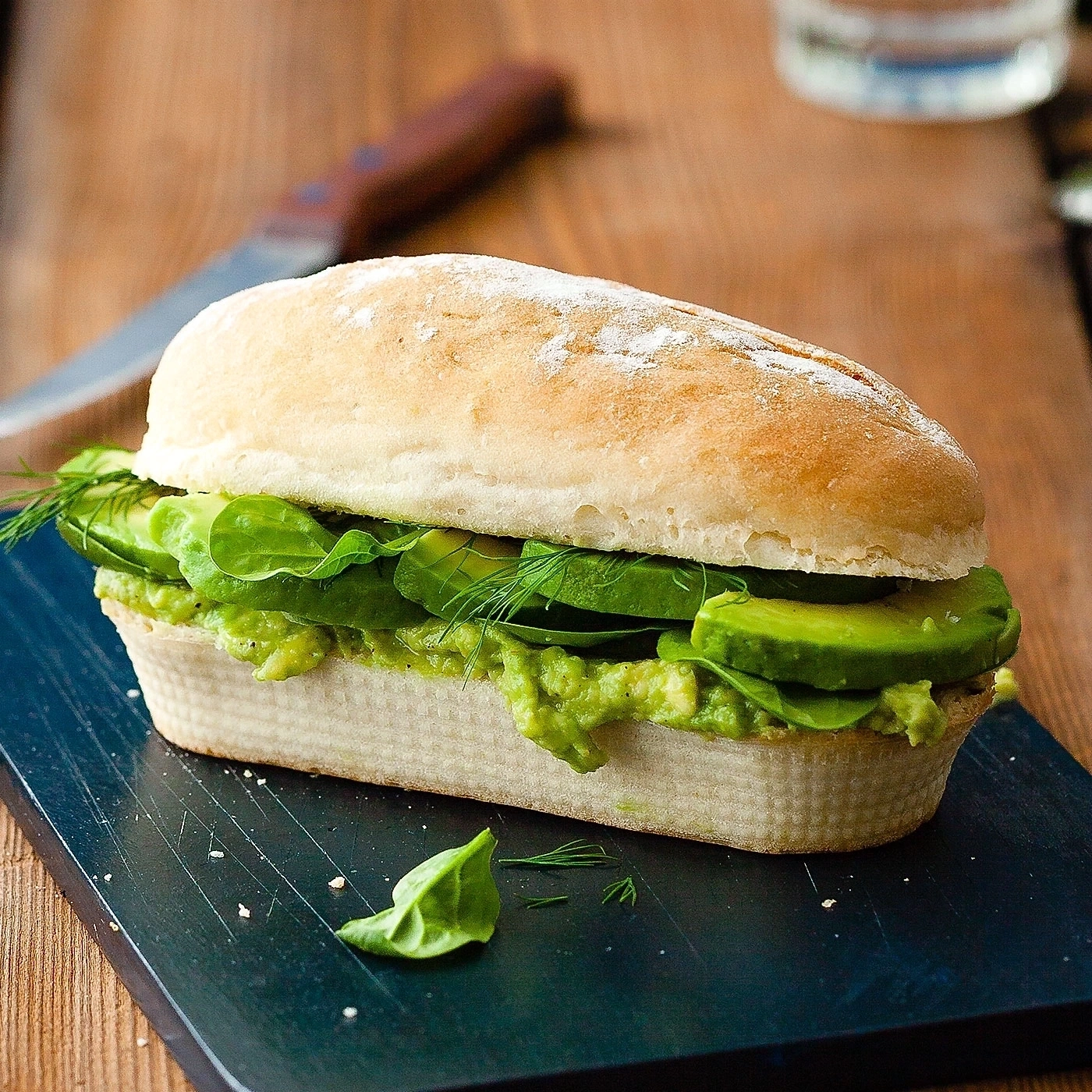 Avocado-Sandwich auf einem schwarzen Brett, mit Dill und Salat.