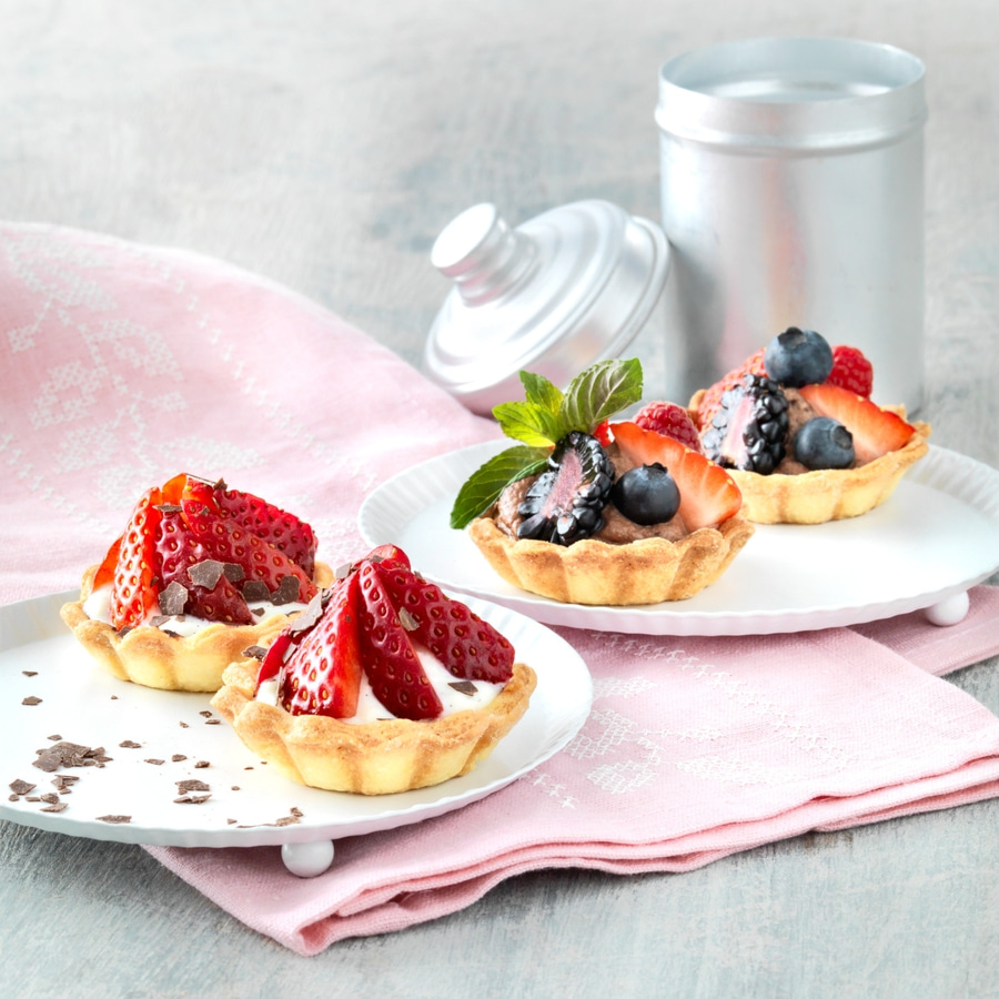 Köstliche Obsttörtchen auf Tellern, mit Erdbeeren, Blaubeeren und Brombeeren dekoriert.