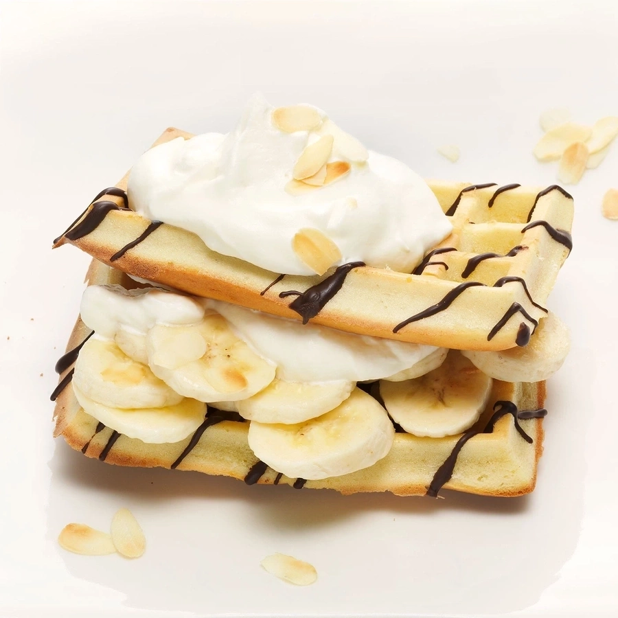 Waffel mit Bananen, Sahne, Schokosauce und Mandelsplittern auf weißem Teller
