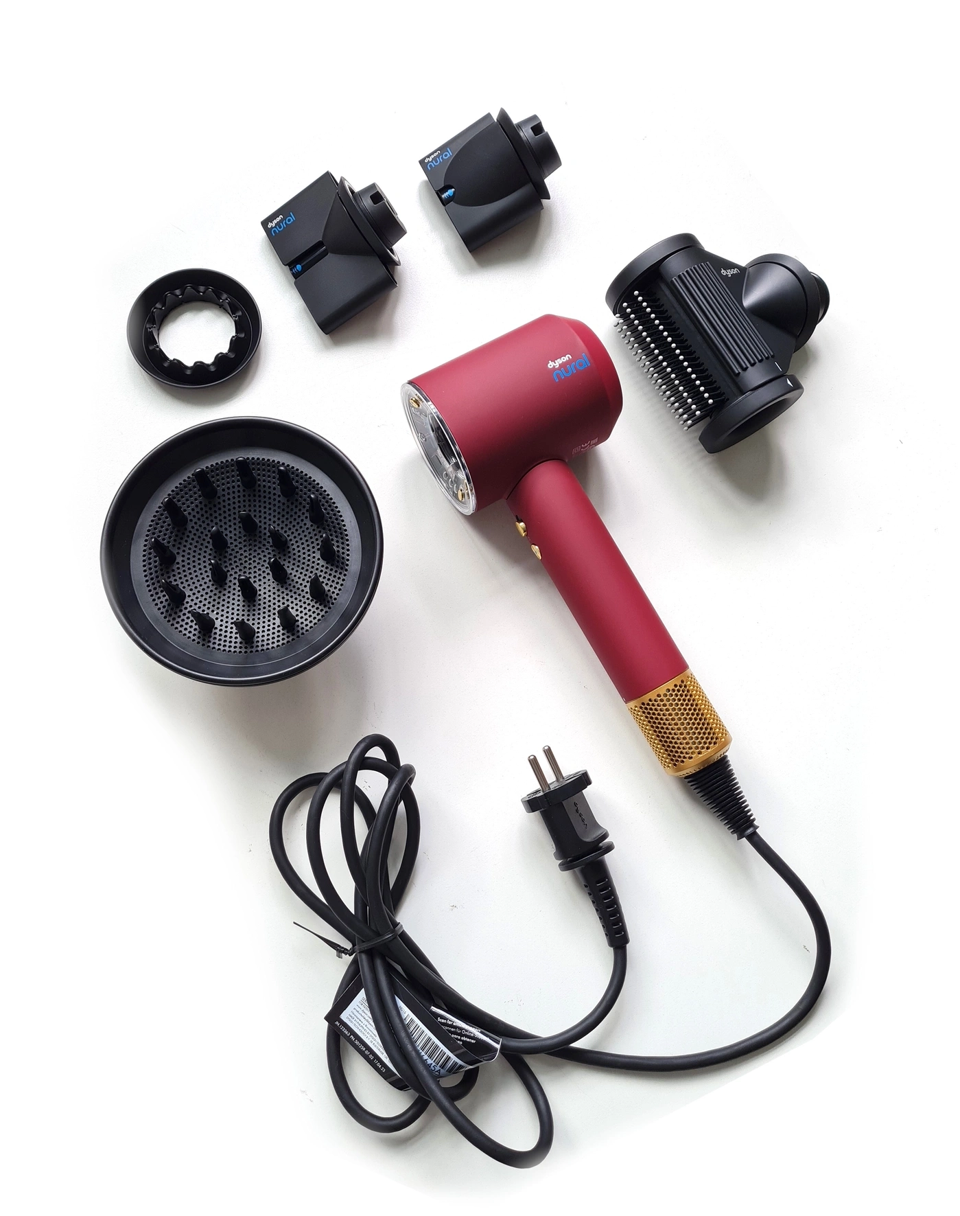 Roter Dyson Haartrockner mit Zubehör und Kabel auf weißem Hintergrund.