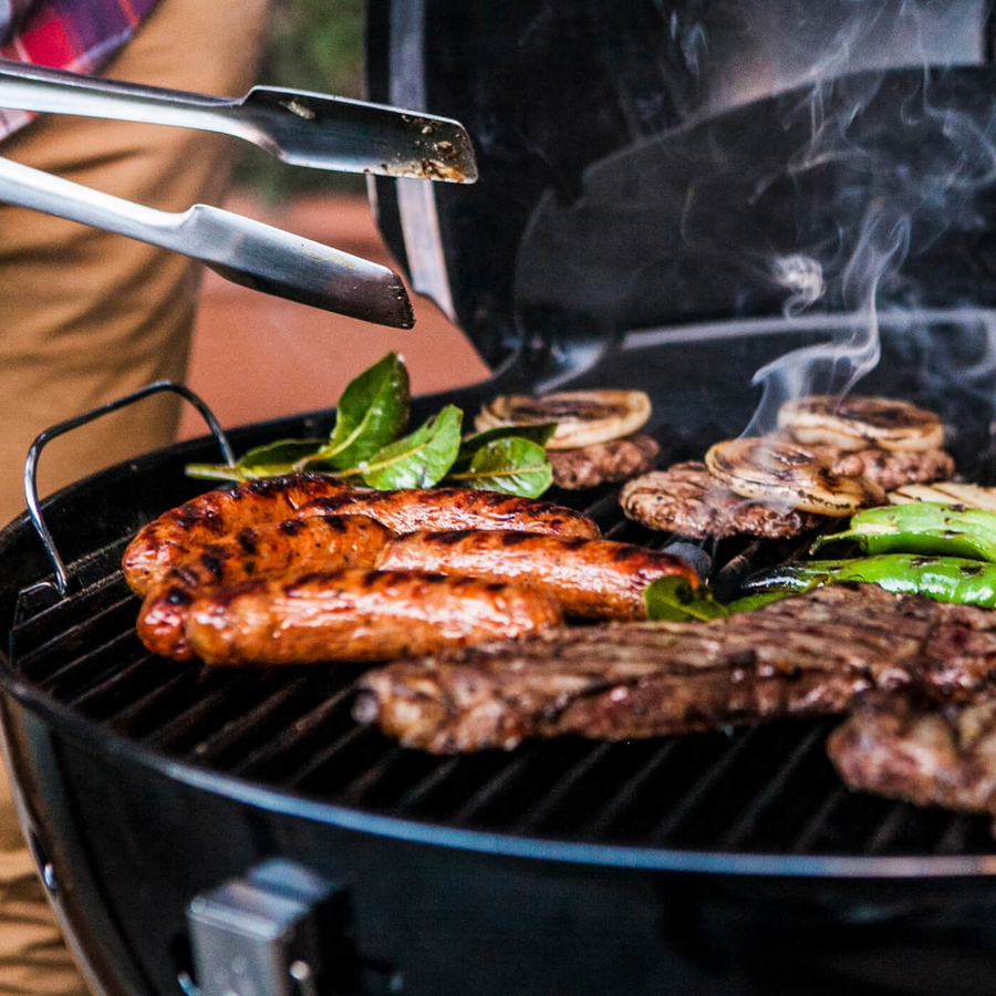 Grill mit Würstchen, Steak, Gemüse und Grillzange, raucht.