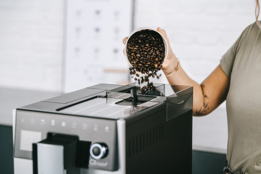 Kaffeebohnen werden in eine Kaffeemaschine gegossen, Nahaufnahme, Person