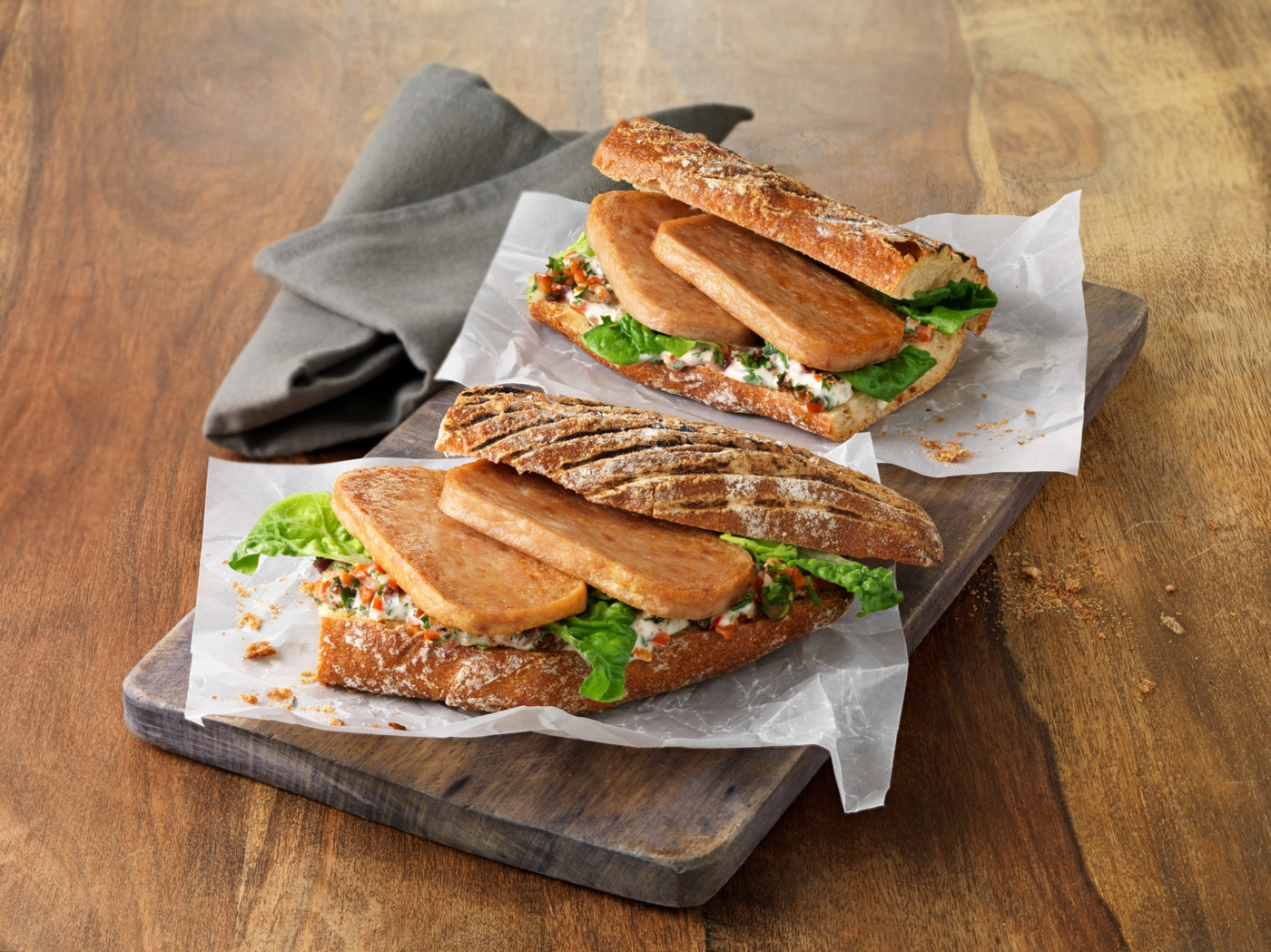 Zwei Sandwiches auf einem Holzbrett mit Salat und Fleisch