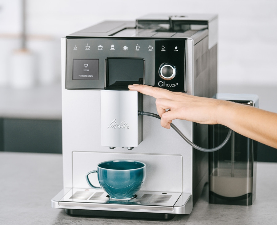 Kaffeemaschine mit Touch-Funktion und Tasse. Eine Hand berührt die Maschine.