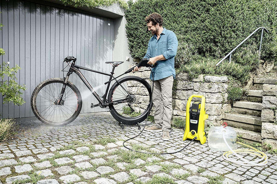 Mann reinigt Fahrrad mit Hochdruckreiniger im Garten, sonniges Wetter