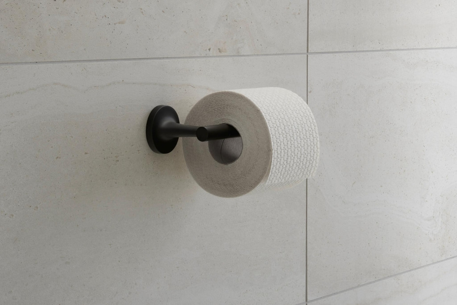 Toilettenpapierhalterung mit Rolle vor hellen Fliesen. Schwarze Halterung.