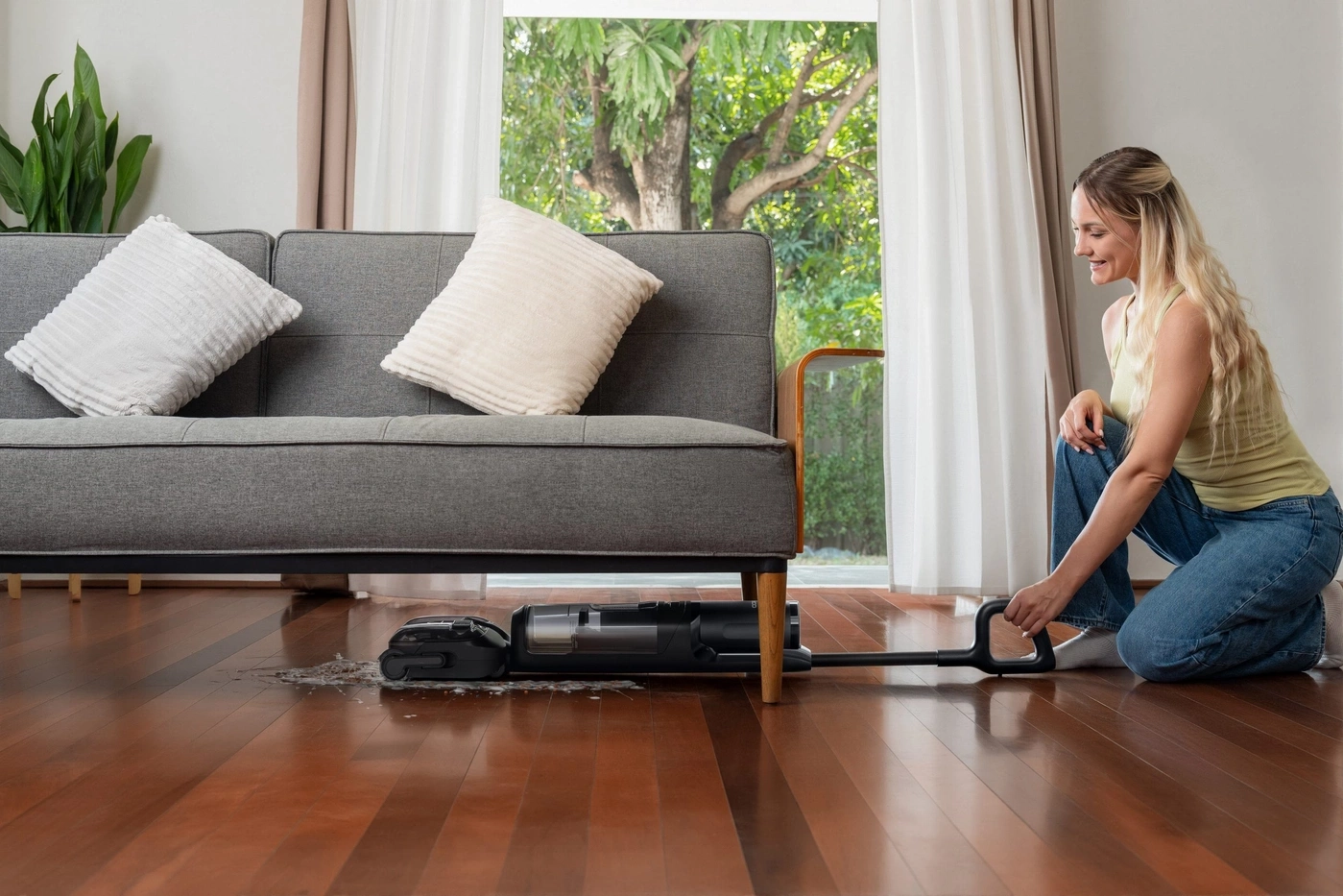 Frau benutzt Nass-/Trockensauger unter dem Sofa für verschüttete Flüssigkeiten.