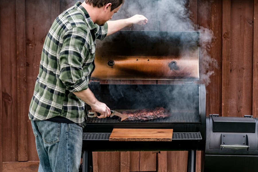 Mann grillt Fleisch auf einem Smoker im Freien, Rauch steigt auf