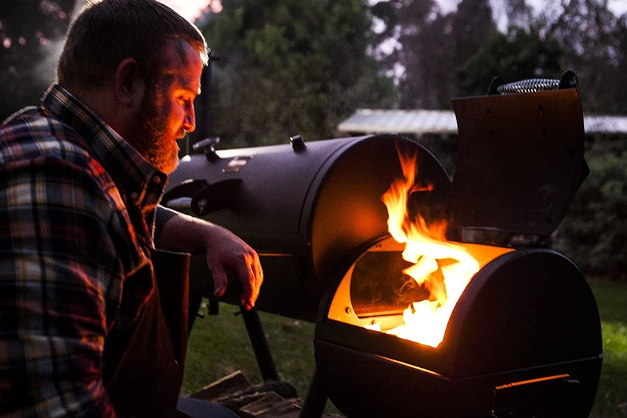 Mann am Grill mit Flammen, die aus dem Grill kommen, Abendessen im Freien