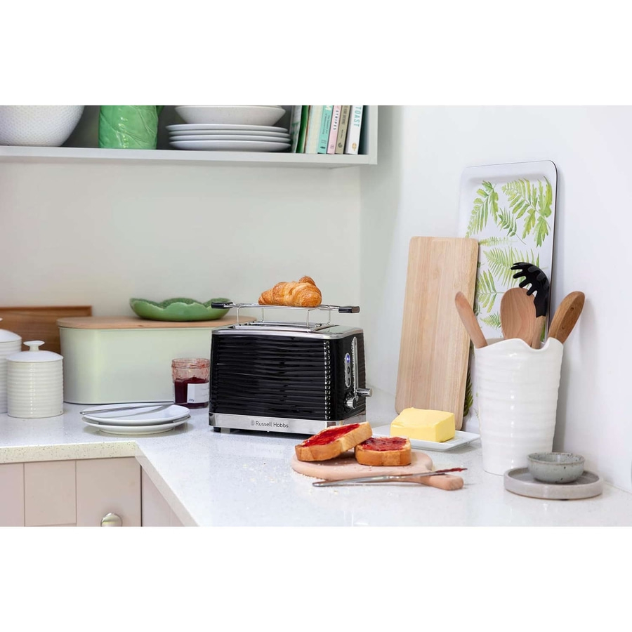Ein Toaster mit Croissant, Brot, Butter und Küchenutensilien auf einer Arbeitsplatte.