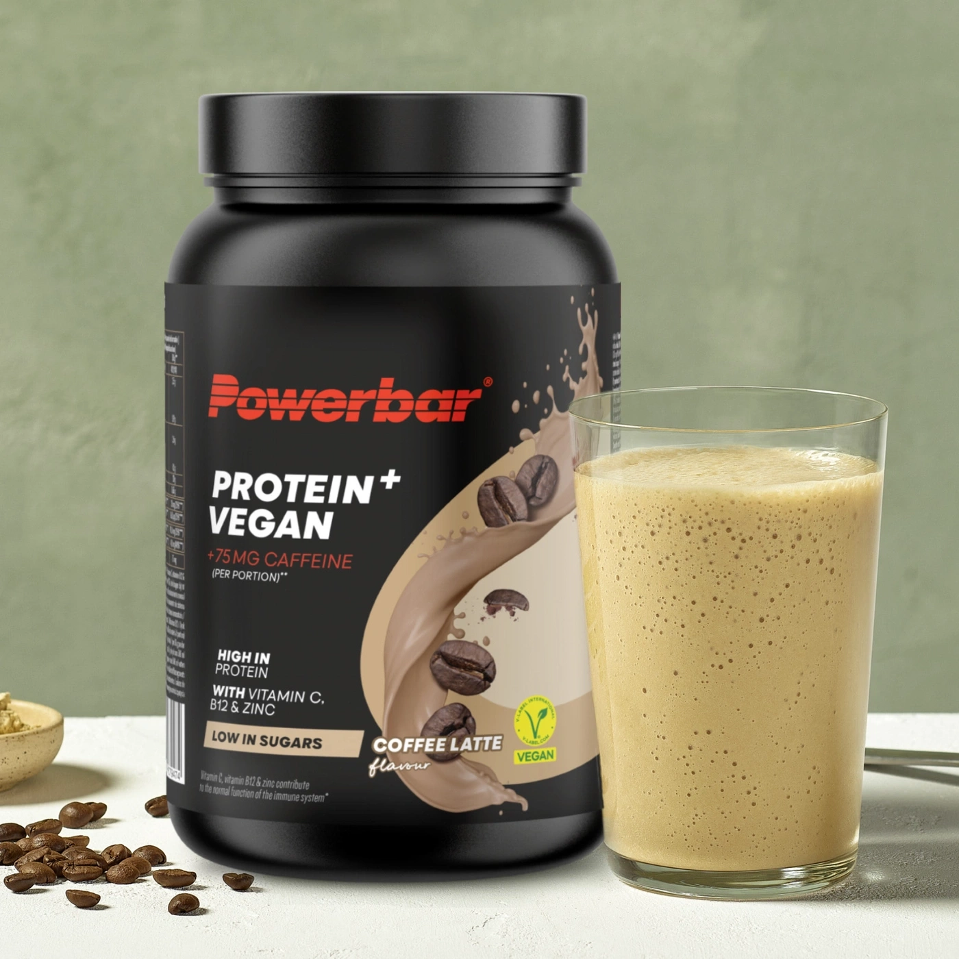 Powerbar Protein Vegan in Kaffee Latte Geschmack neben einem Glas Proteinshake.