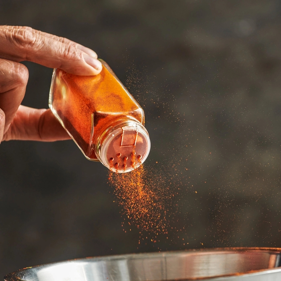 Person streut Gewürz aus einem Glasbehälter in eine Schüssel