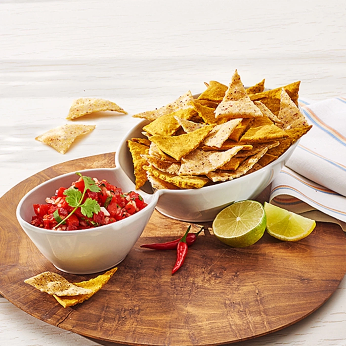 Schüssel mit Tortilla-Chips, Salsa, Limette und Chili auf Holzbrett