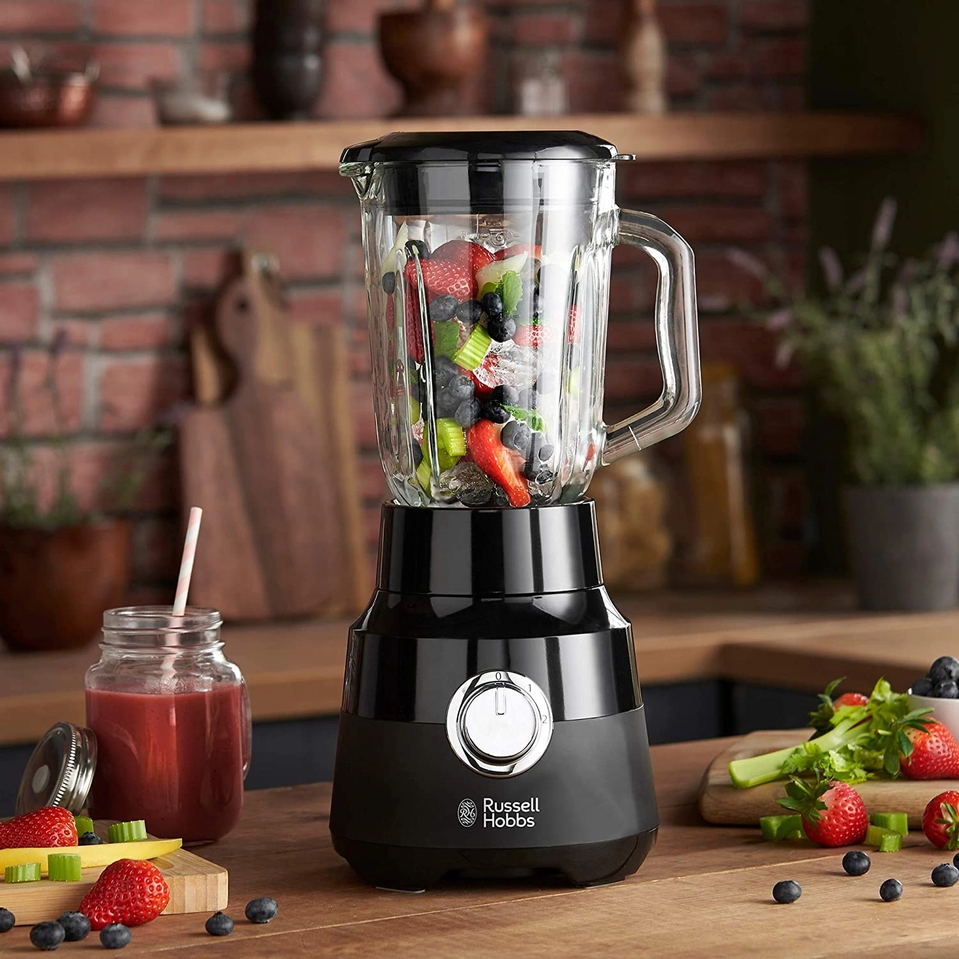 Ein schwarzer Mixer mit Früchten und einem Glas Saft daneben