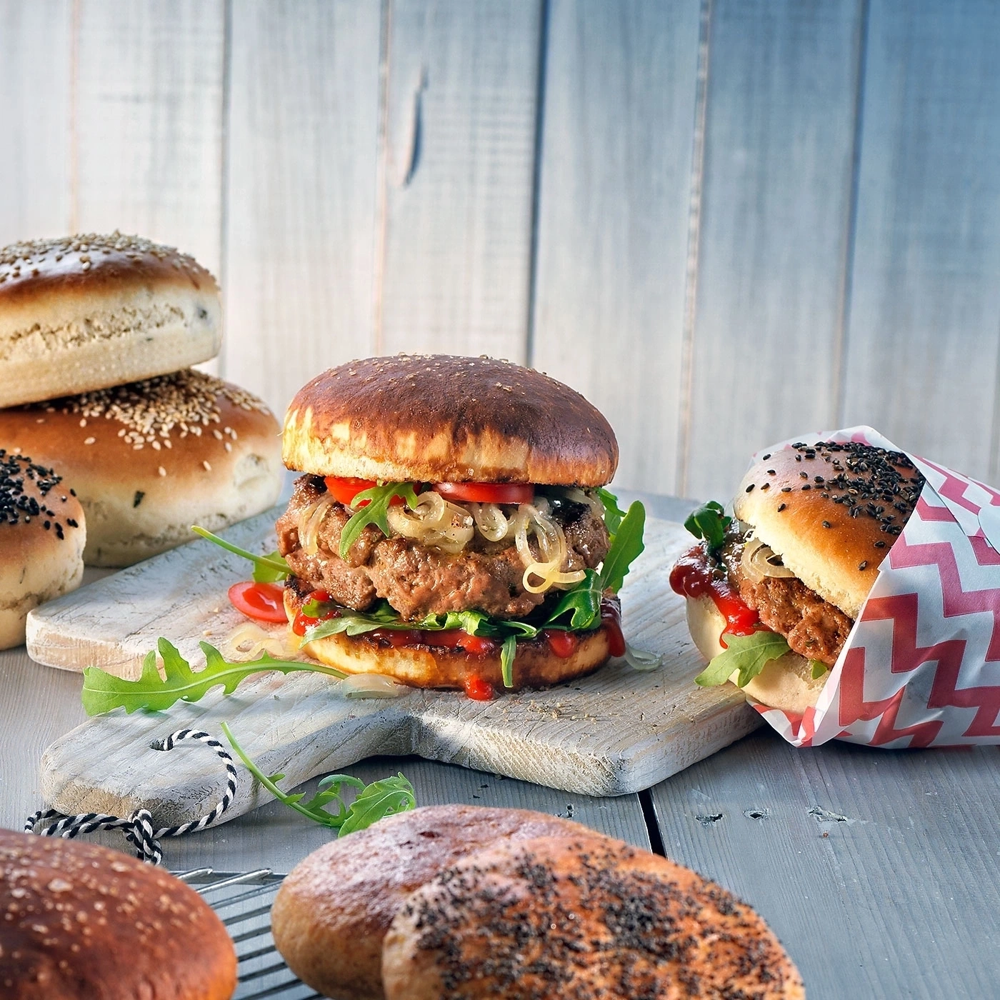 Burger mit Tomaten, Zwiebeln und Salat auf einem Holzbrett