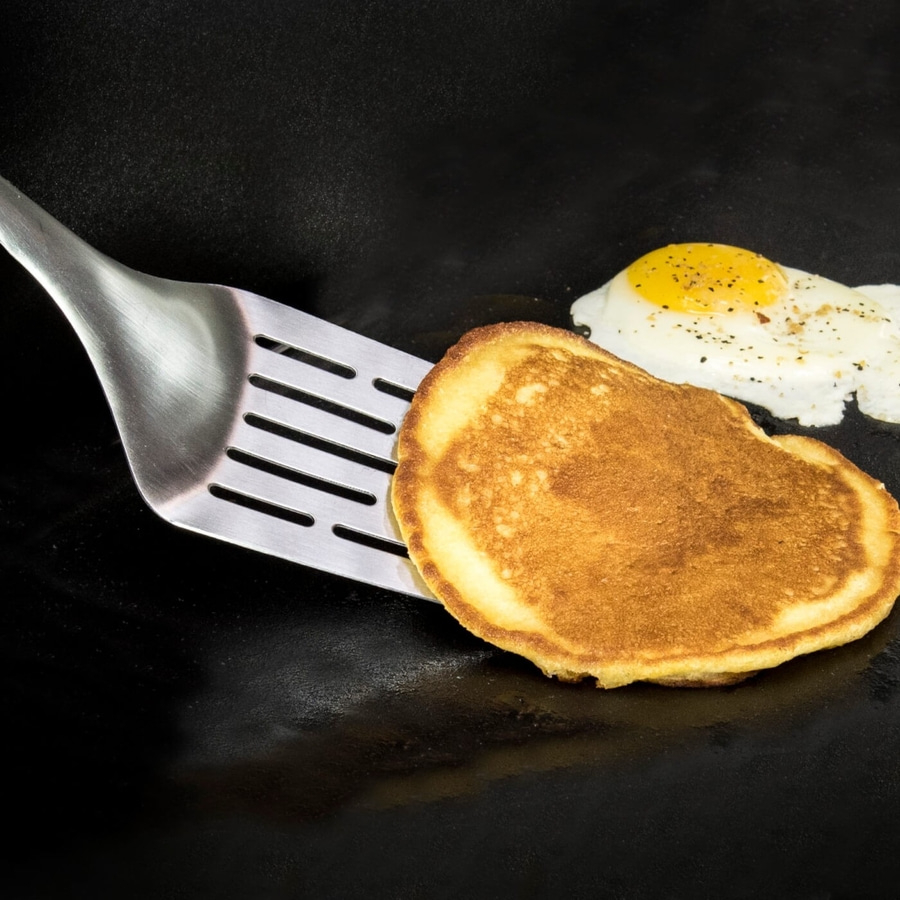 Pfannkuchen und Spiegelei auf einer schwarzen Kochfläche mit Pfannenwender