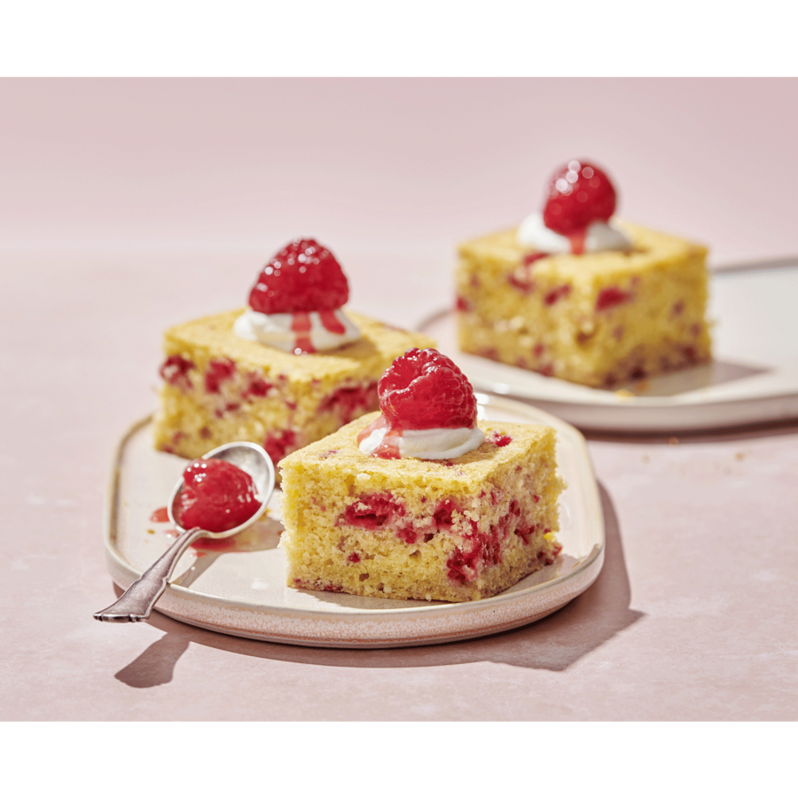 Kuchenstücke mit Himbeeren und Sahne auf Tellern, Löffel mit Marmelade