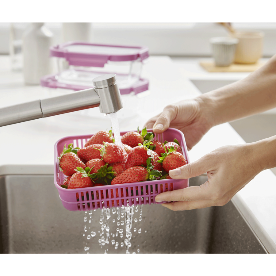Erdbeeren werden in einem rosa Sieb unter fließendem Wasser gewaschen.