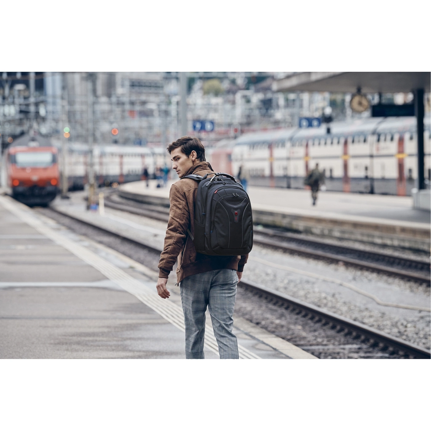 Ein Mann mit Rucksack steht am Bahnhof und schaut auf die Züge.