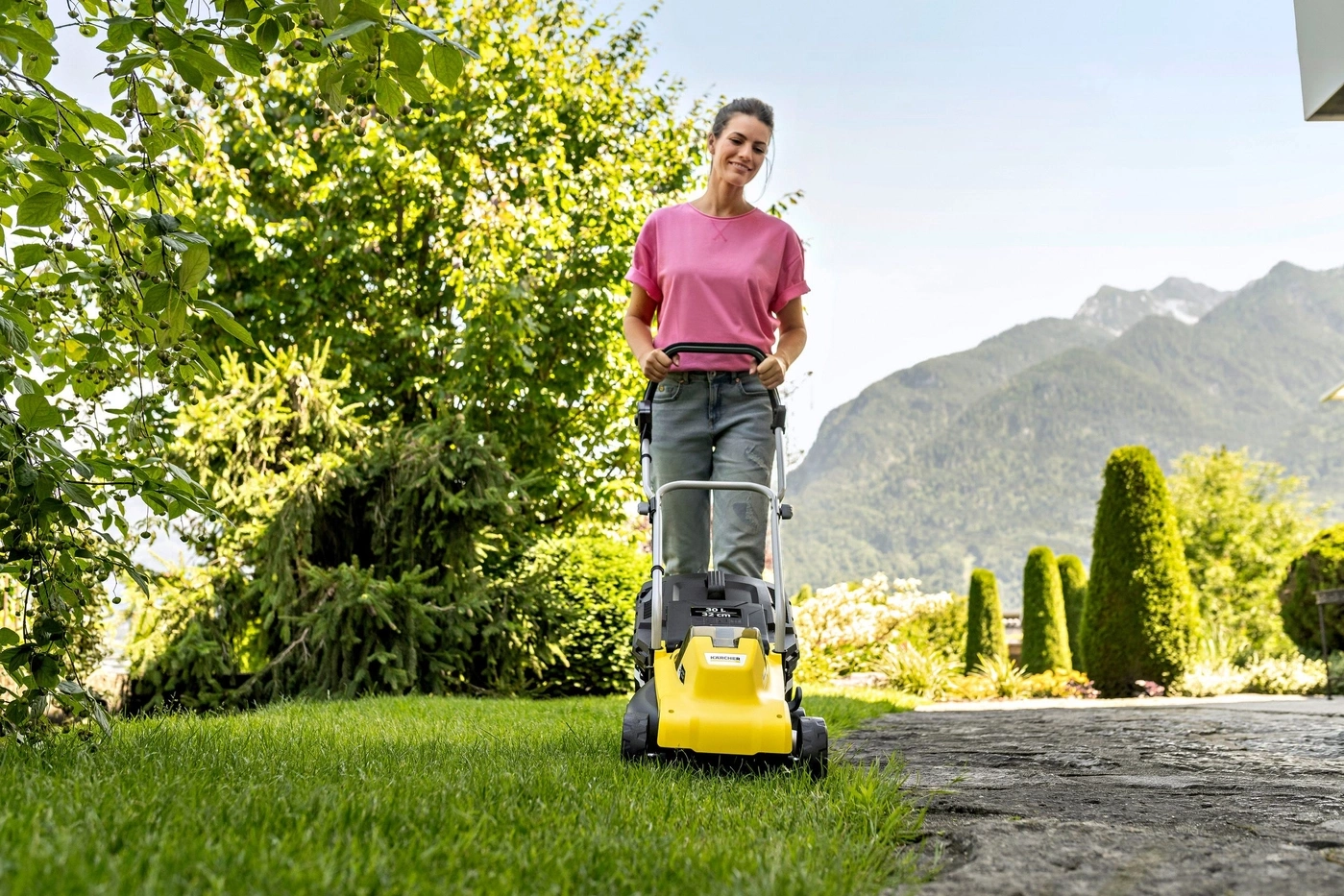 Eine Frau mäht mit einem gelben Rasenmäher im Garten