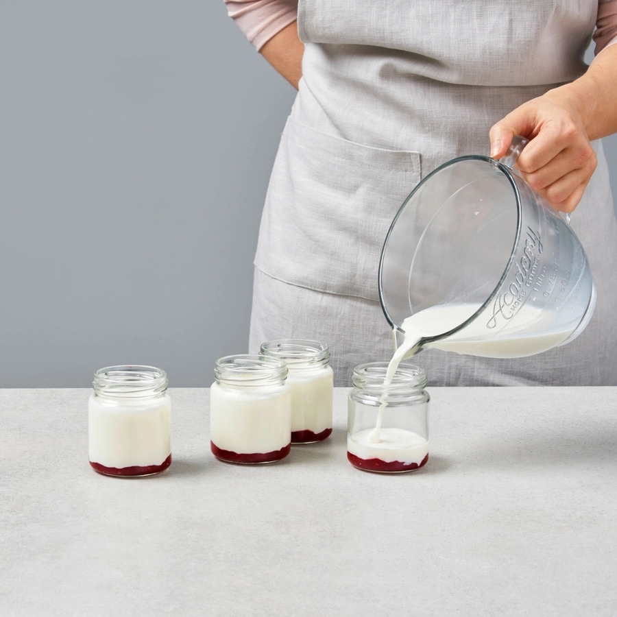 Jemand gießt Milch in Gläser mit roter Schicht. Joghurt Zubereitung.