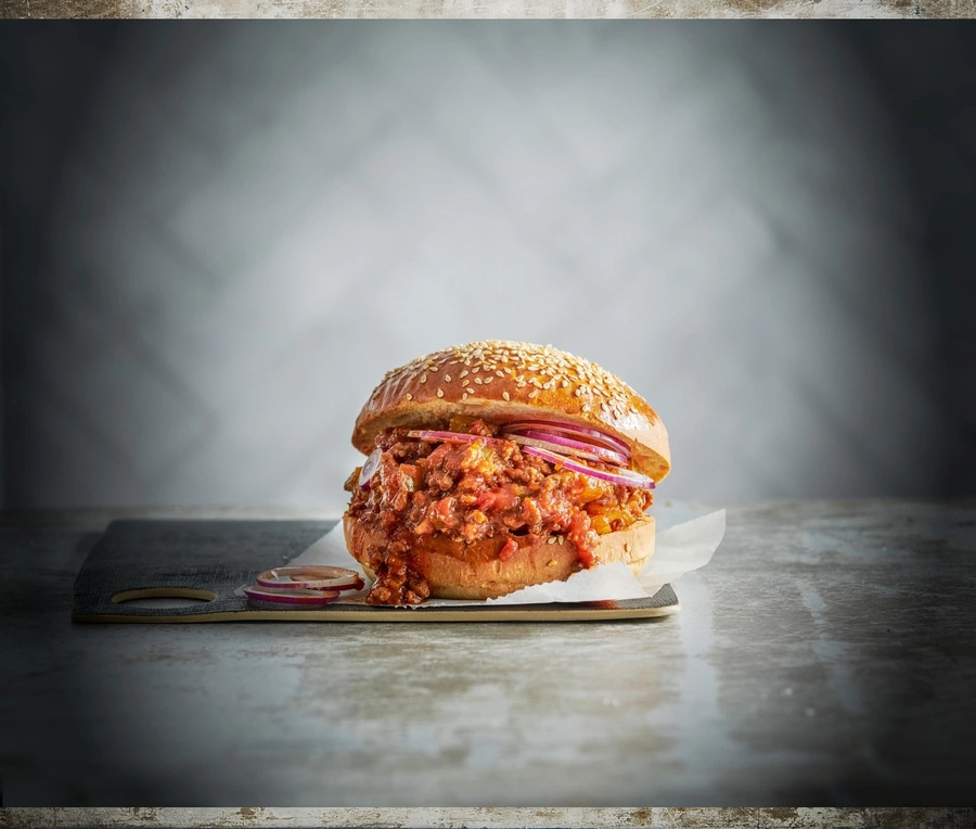 Ein köstlicher Burger mit Fleisch, Zwiebeln und Sesambrötchen auf einem Brett.