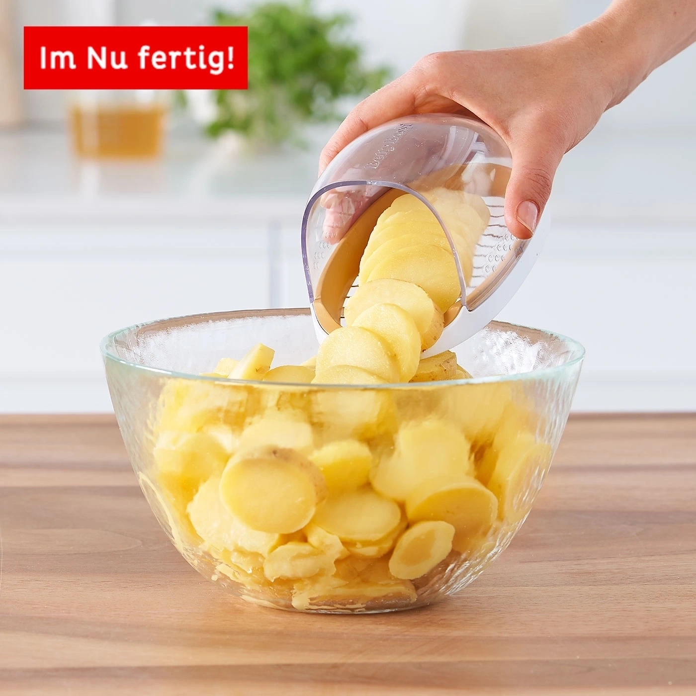 Kartoffelscheiben werden in eine Glasschüssel geschnitten. Eine Hand hält einen Kartoffelschneider.