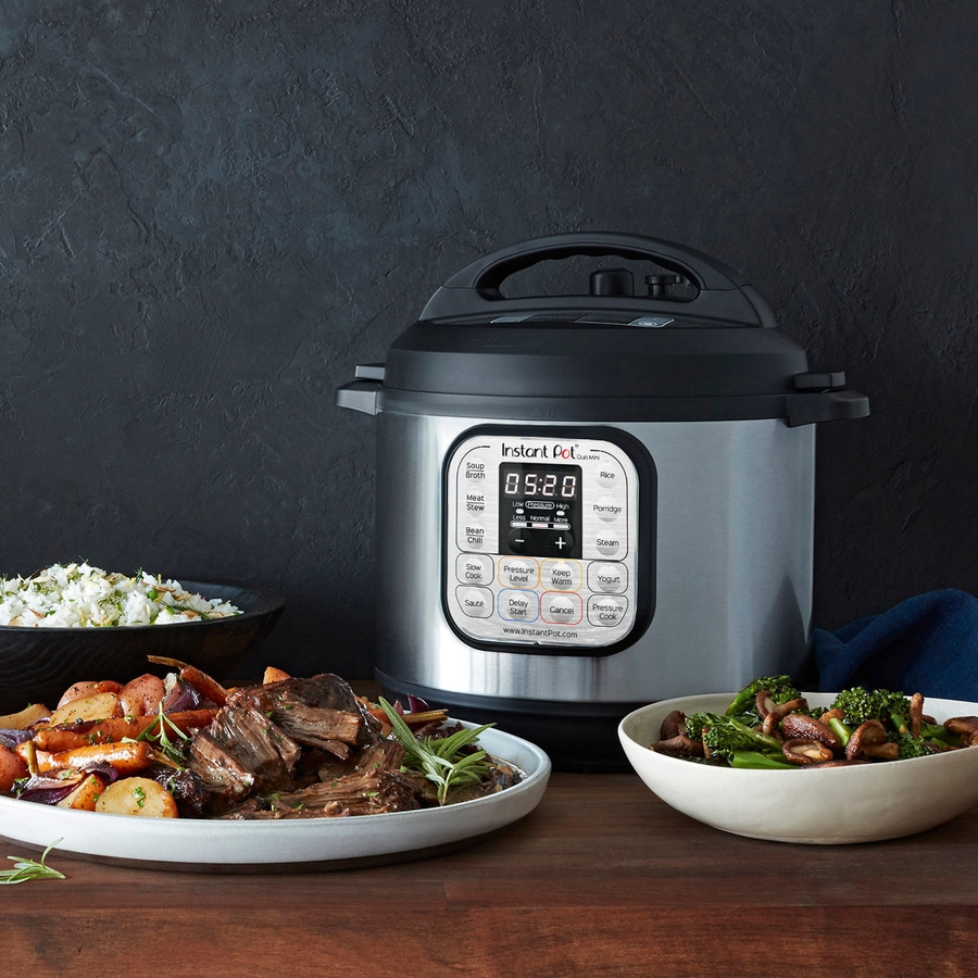 Instant Pot mit Essen, Gemüse und Fleisch auf einem Holztisch vor dunklem Hintergrund.