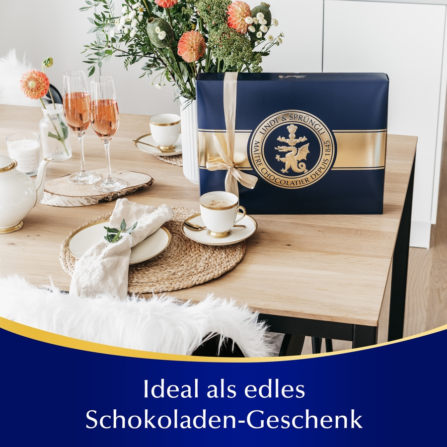 Ein Lindt & Sprüngli Schokoladen-Geschenk auf einem Tisch mit Champagnergläsern und Blumen.