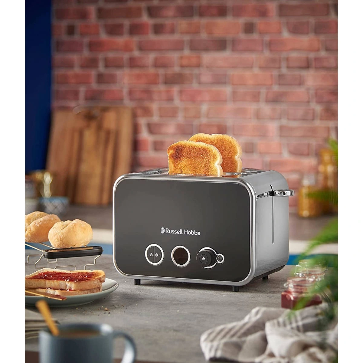Ein schwarzer Toaster mit zwei Toastscheiben, daneben Brot und Marmelade.
