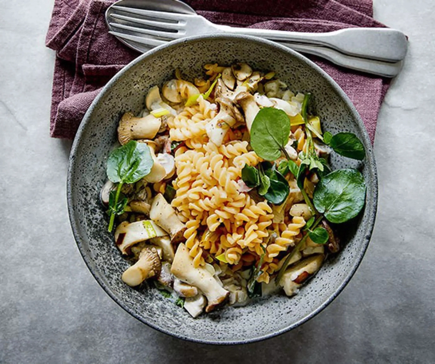Pasta mit Pilzen und Kräutern in einer Schüssel auf einem Tisch mit einer Serviette und Besteck