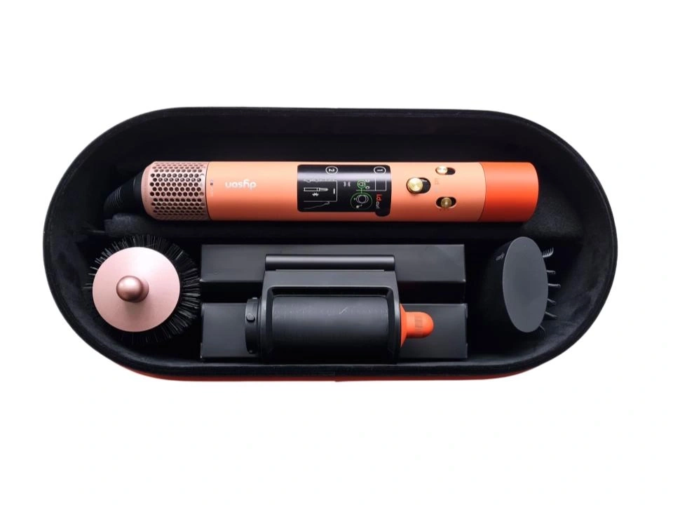Ein orangefarbener Dyson Haarglätter mit Zubehör in einem schwarzen Koffer.