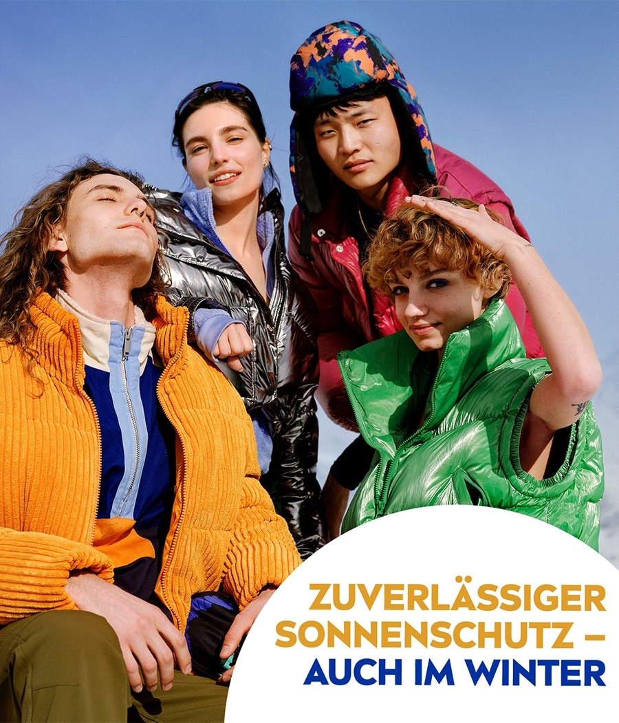 Vier junge Menschen in Winterkleidung, die vor blauem Himmel posieren.