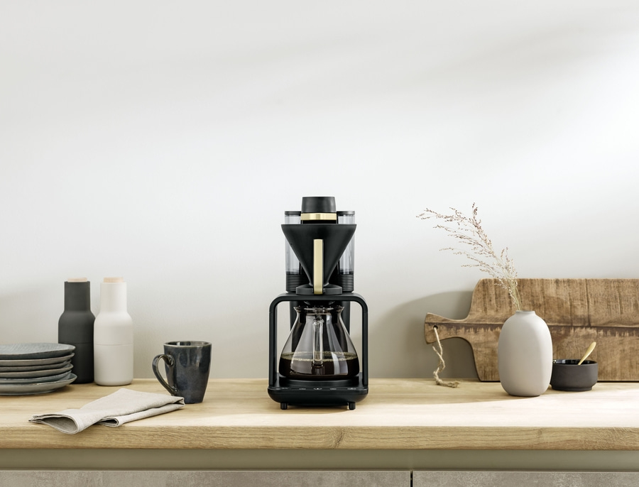 Kaffeemaschine auf einer Holzoberfläche mit Dekoration und Zubehör in einem hellen Raum.