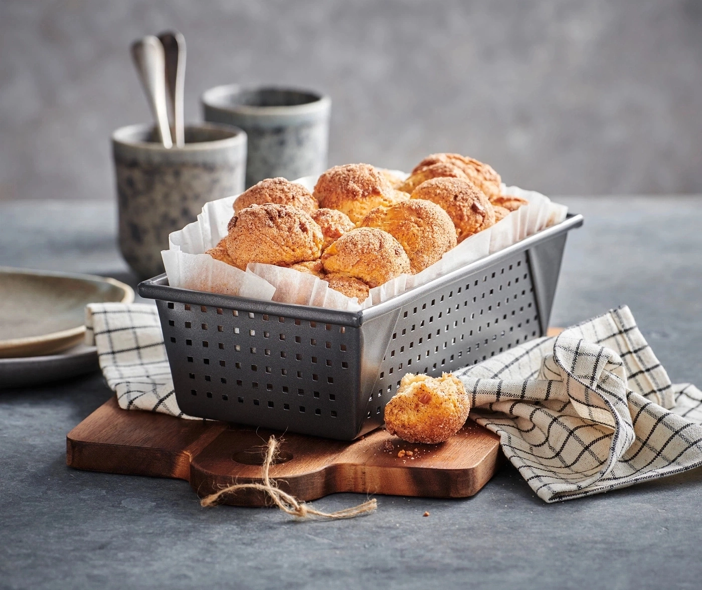Korb mit Gebäck auf Holzbrett, daneben ein zerbrochenes Gebäckstück und ein Tuch.
