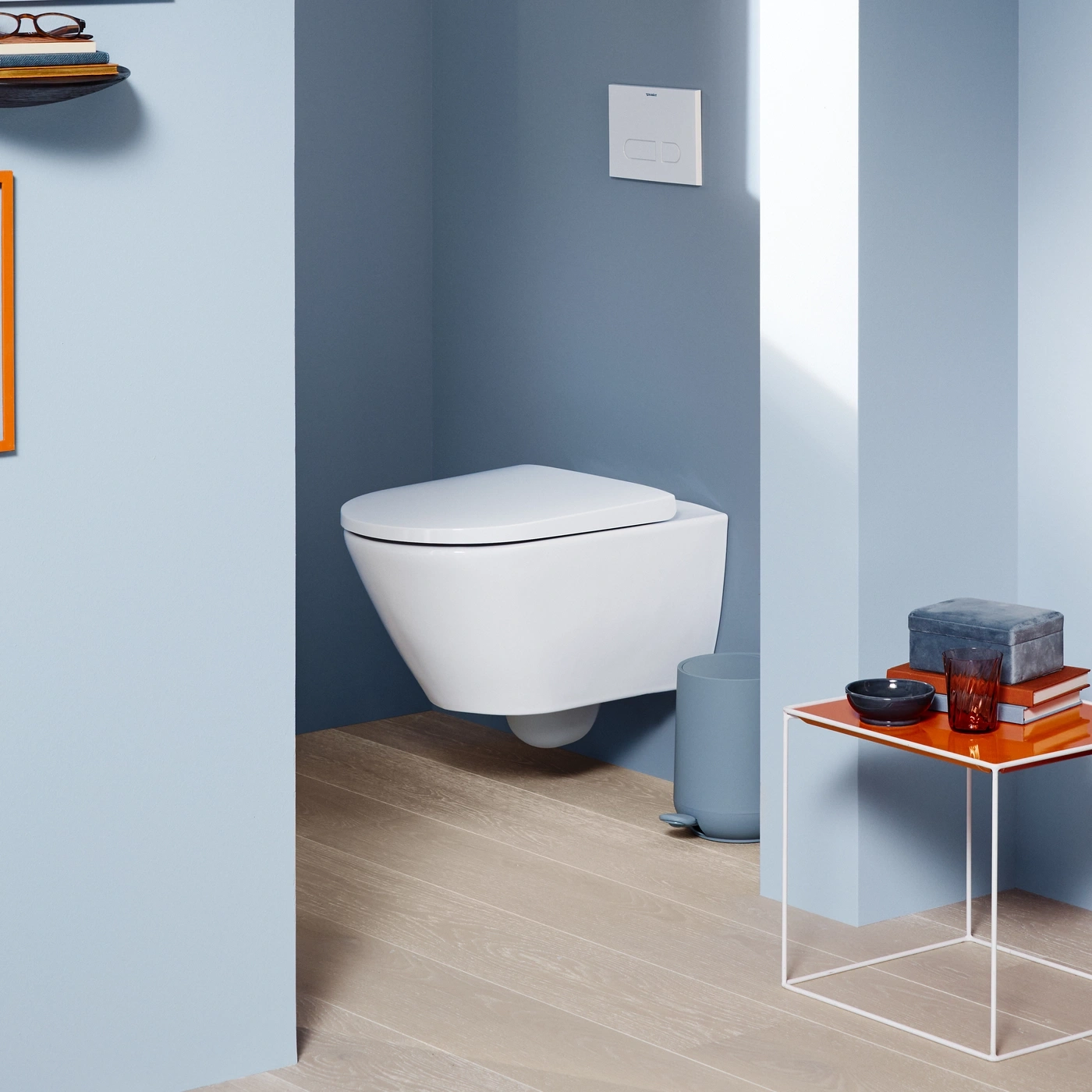Ein modernes Badezimmer mit wandhängender Toilette und einem Beistelltisch mit Dekoration.