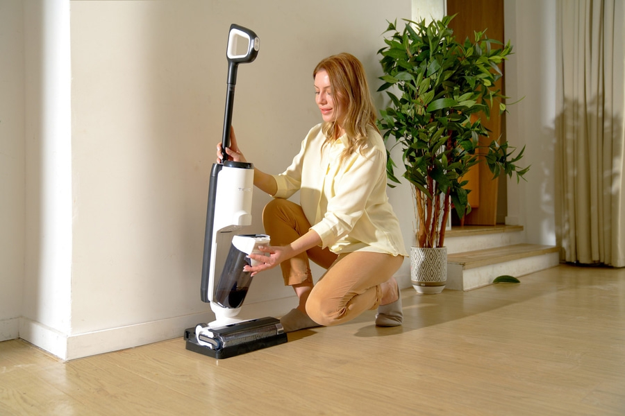 Frau mit Staubsauger, kniend, Haus, Reinigung, helles Outfit, Zimmerpflanze, Holzfußboden, Licht