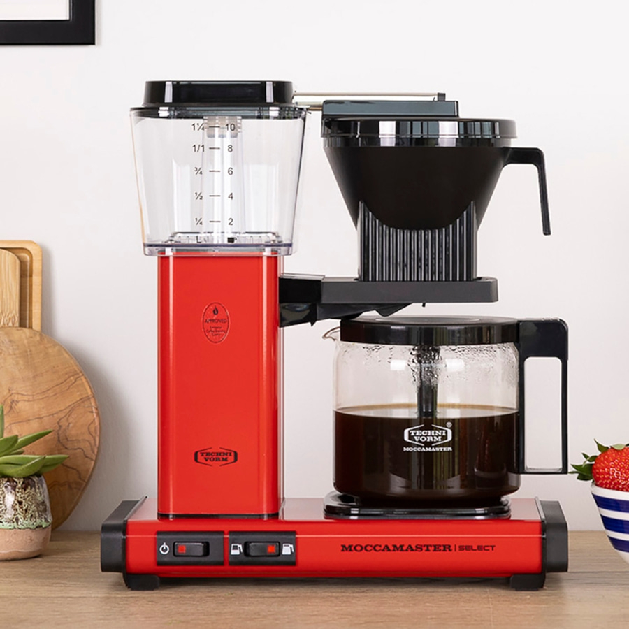 Rote Moccamaster Kaffeemaschine mit Glaskanne und Messbecher, perfekt für Kaffee-Liebhaber.