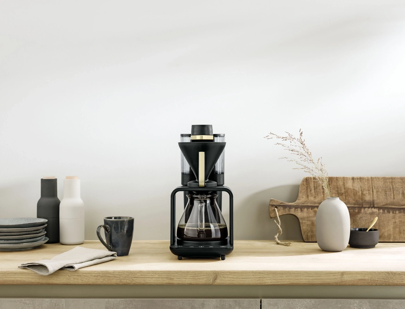 Kaffeemaschine auf einer Holzoberfläche mit Dekoration und Zubehör in einem hellen Raum.